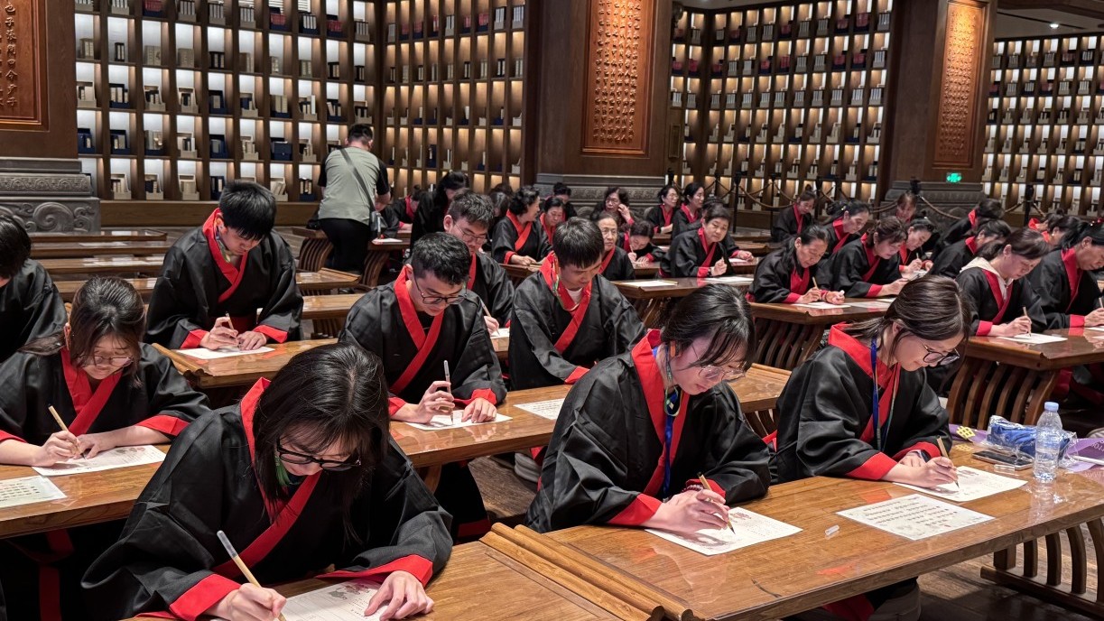 Students on the exchange programme dressed in traditional Chinese clothing copy The Analects with calligraphy brushes in the University Hall of Nishan Sacred Land.