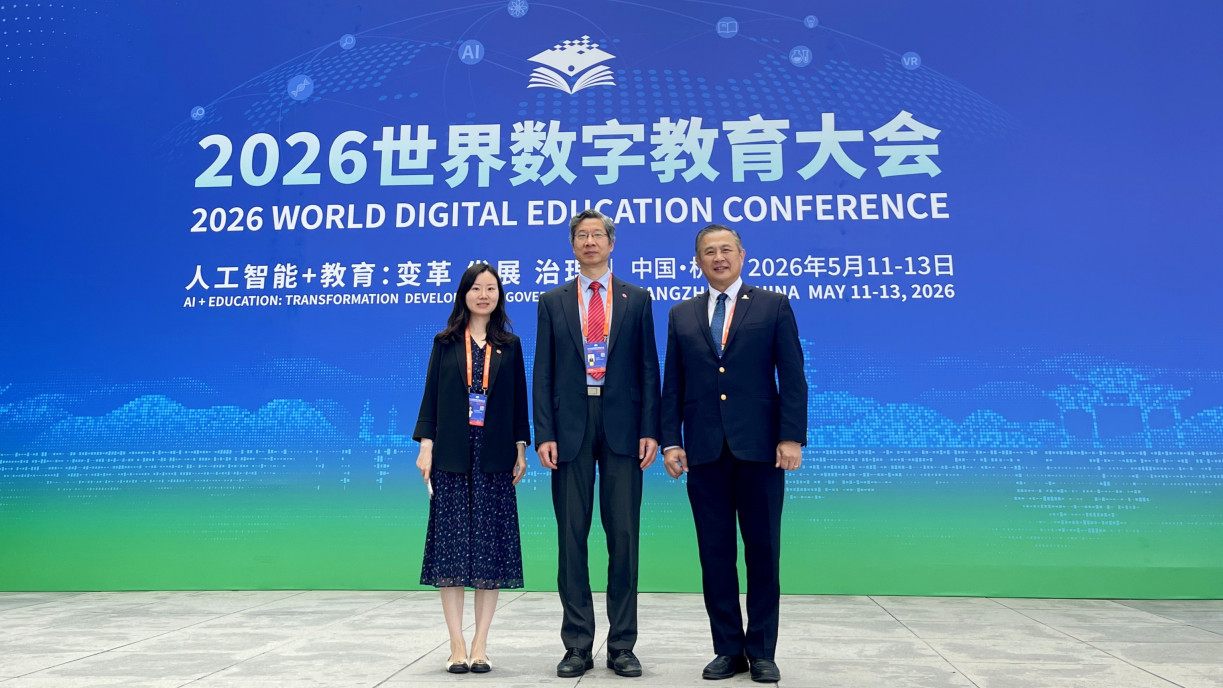两位岭大参会代表在2026世界数字教育大会的大型蓝色背景墙前与一位嘉宾合影留念