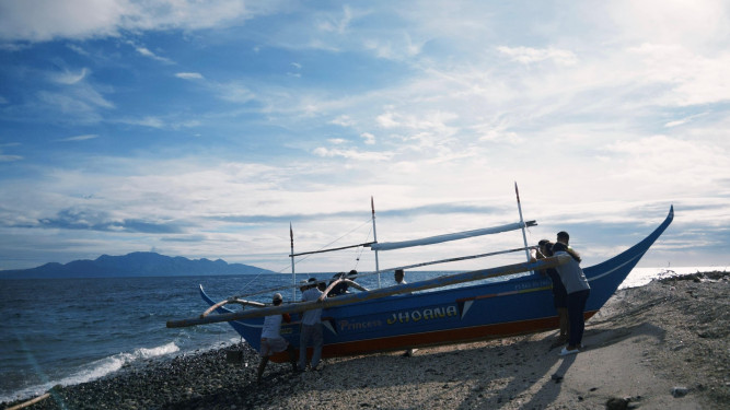  People launching a blue outrigger boat named Princess JHOANA from a beach.