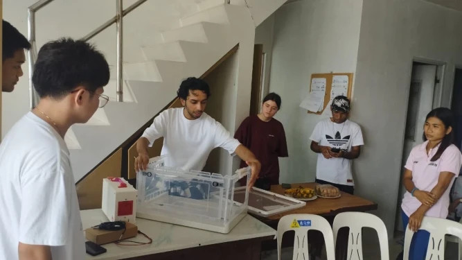  Student researcher assembling the portable baby incubator prototype while onlookers watch.