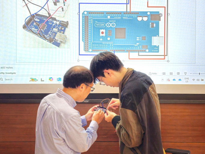  Instructor and student troubleshooting an Arduino microcontroller circuit in front of a presentation screen.