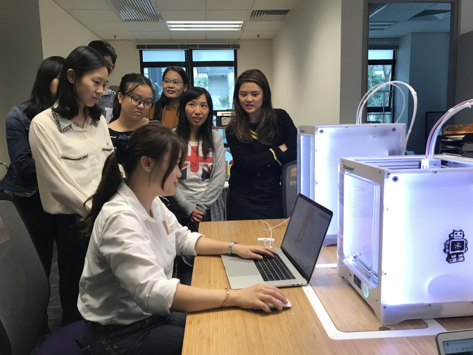 Instructor demonstrating 3D printing setup to students in a lab.