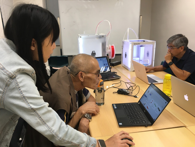 Instructor assisting an elderly participant with 3D design software at a laptop.