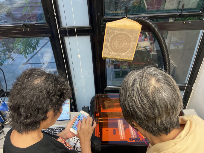  Two participants preparing a job on an laser cutter using a smartphone and laptop.