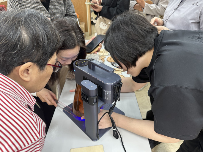  Participants closely watching a portable laser engraver during a workshop demonstration.