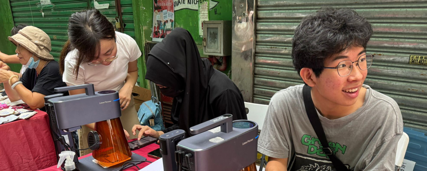 Students and community members creating custom laser-engraved products at an outdoor market stall.