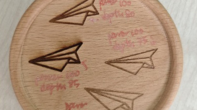 Laser engraving parameter test of paper airplane icons on a round wooden coaster.