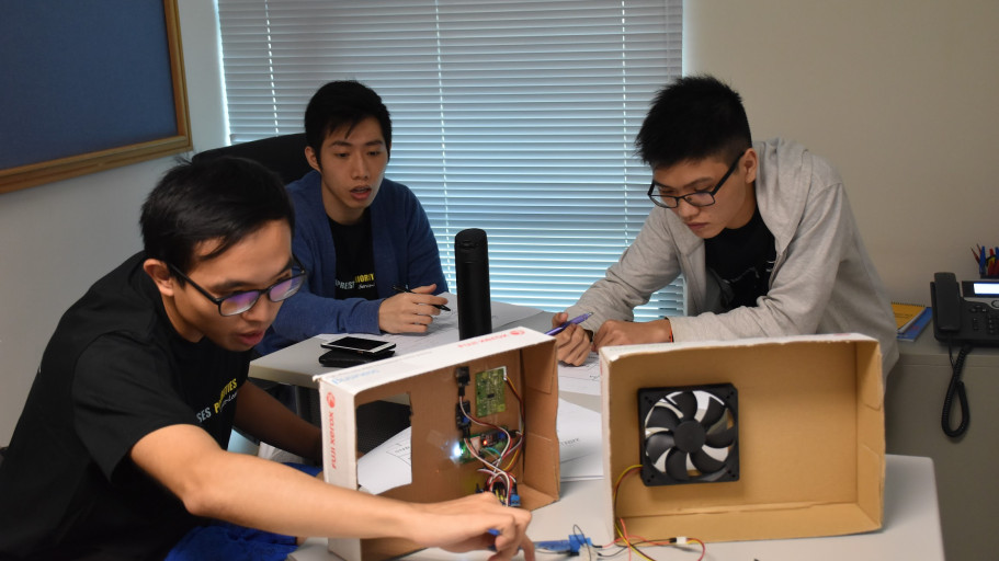  Students reviewing and testing a cardboard electronic enclosure prototype in an office setting.