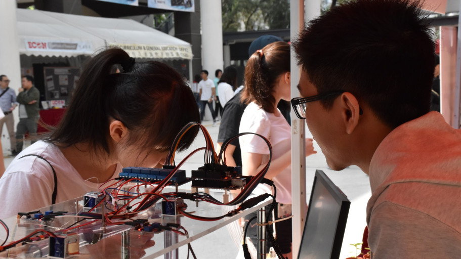  Students examining an electronics and relay module project prototype at a campus showcase.