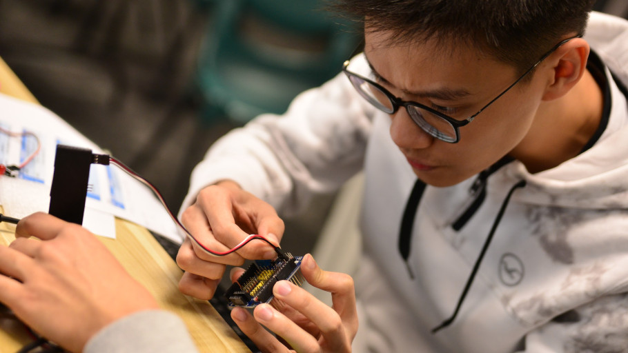  Student focusing on wiring a microcontroller expansion board during a lab session.