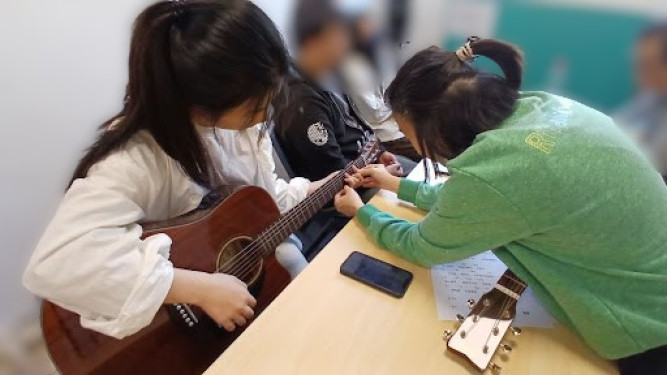 A photo showing Maggie teaching a Lingnan University student Guitar.